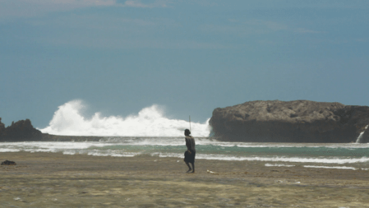 Kokoly walks along the reef, crashing waves in the background